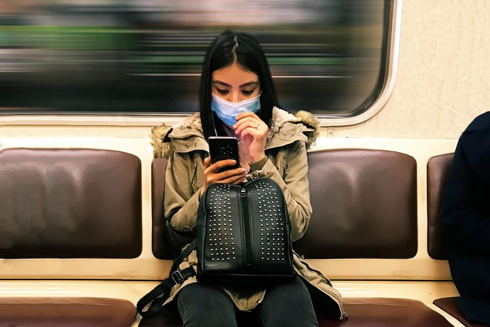 Young woman wearing a medical mask in subway train while texting on mobile phone