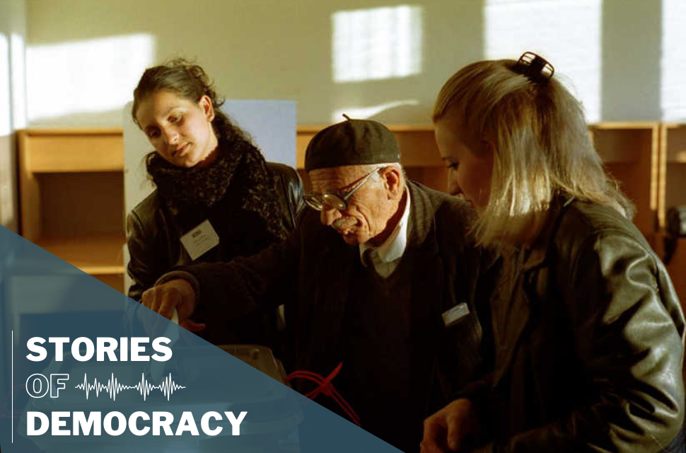Election supervisors from the OSCE assisting an elderly voter cast a ballot.