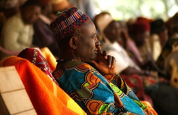 an african man wearing traditional colourful dress sitting and watching during a celebration