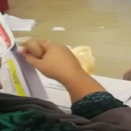 A screenshot from the viral video showing: 1. a person taking a ballot out of an envelope, 2. a stack of ballots sitting on the person’s lap ready to be “dealt with”, 3. the person, using a wooden pick similar-looking to those officially produced, punched the ballot at a particular location, and 4. the person would then put the punched ballot back to the envelope and seals it. Source: viral video on social media made by an unknown person.