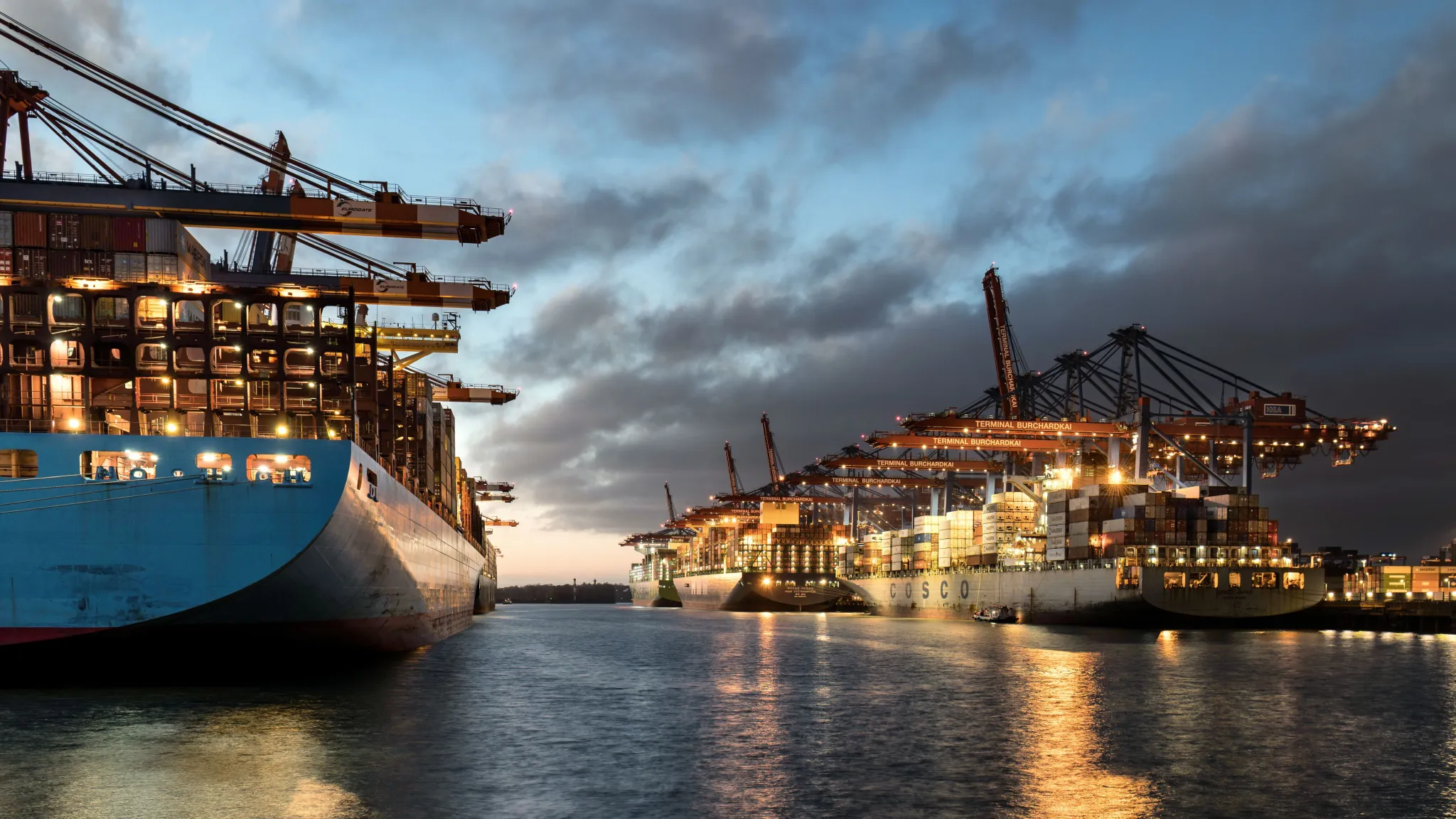 Loaded container ships in a harbor at dusk. Photo by Wolfgang Weiser