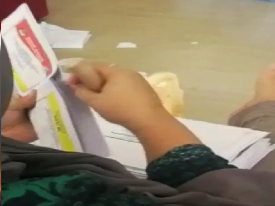 A screenshot from the viral video showing: 1. a person taking a ballot out of an envelope, 2. a stack of ballots sitting on the person’s lap ready to be “dealt with”, 3. the person, using a wooden pick similar-looking to those officially produced, punched the ballot at a particular location, and 4. the person would then put the punched ballot back to the envelope and seals it. Source: viral video on social media made by an unknown person.