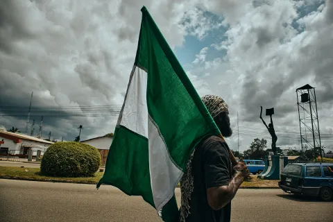 Individual holding a green and white flag in Port Harcourt, Nigeria. Image Credit: Ikwuegbu (@emmages) at Unsplash.